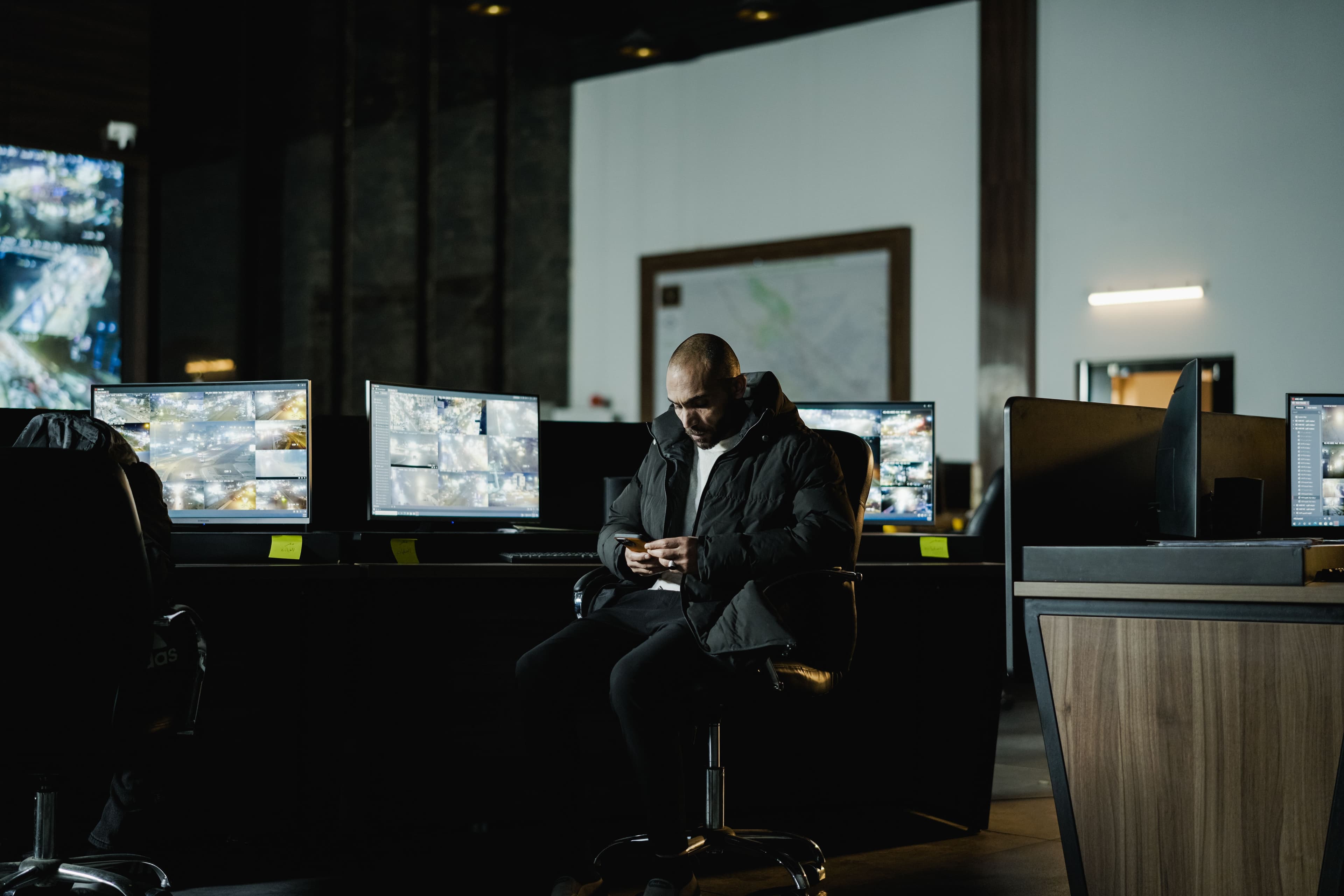 Security operator at a desk in front of a wall of CCTV monitors
